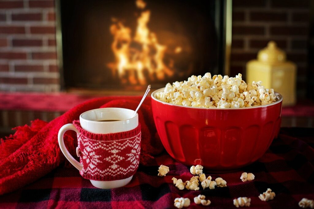 Hot cup of tea in the insualted mug and and popcorns in front of a fire placein front of