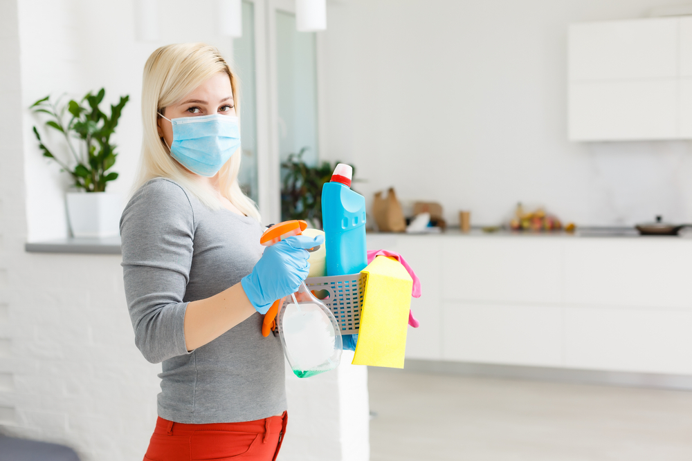 Woman with face mack and load of cleaning products
