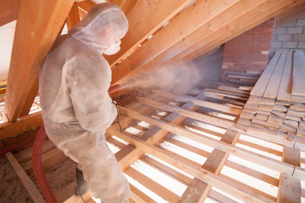 Worker with a hose working on insulation in the attic