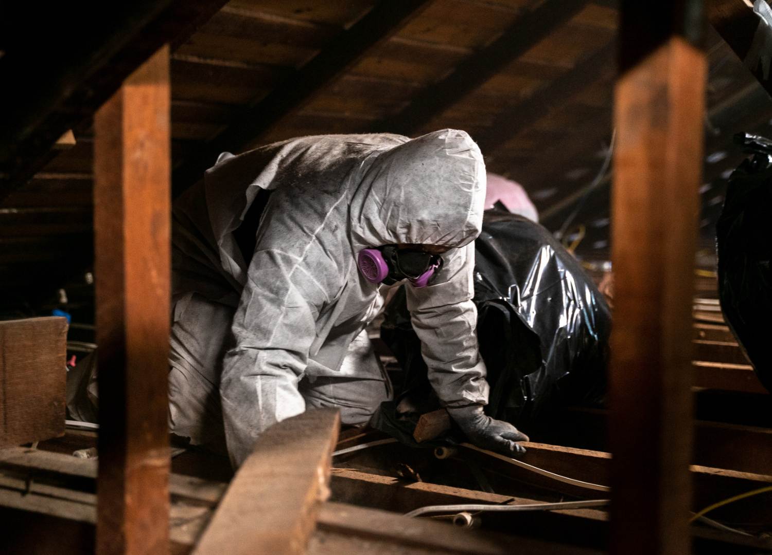man in a white hazard suit and face mask decontaminating an attic.