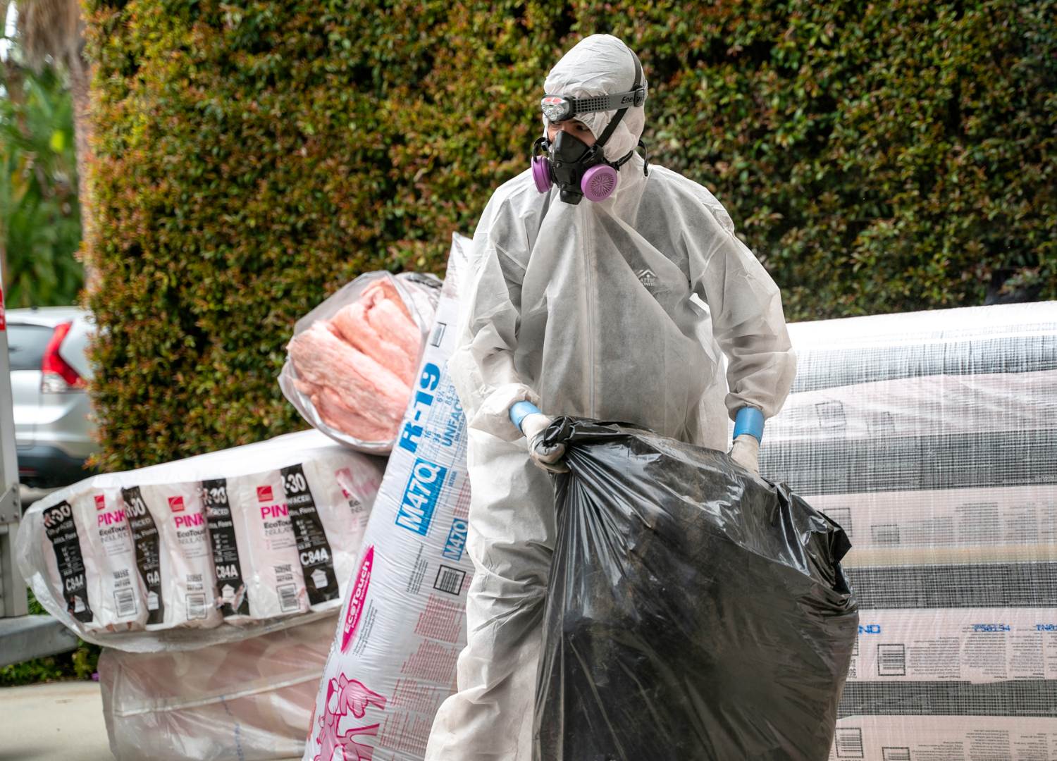 Man in a white hazard suit and face mask decontaminating an attic.