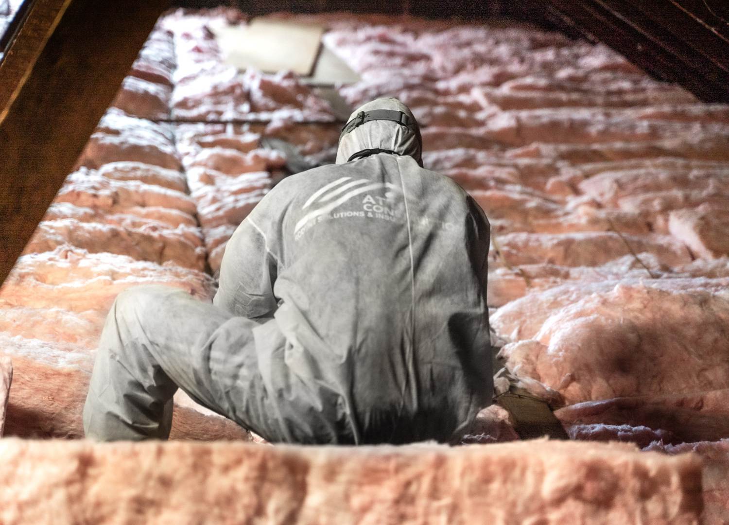 man in a white hazard suit installing new insulation in an attic.