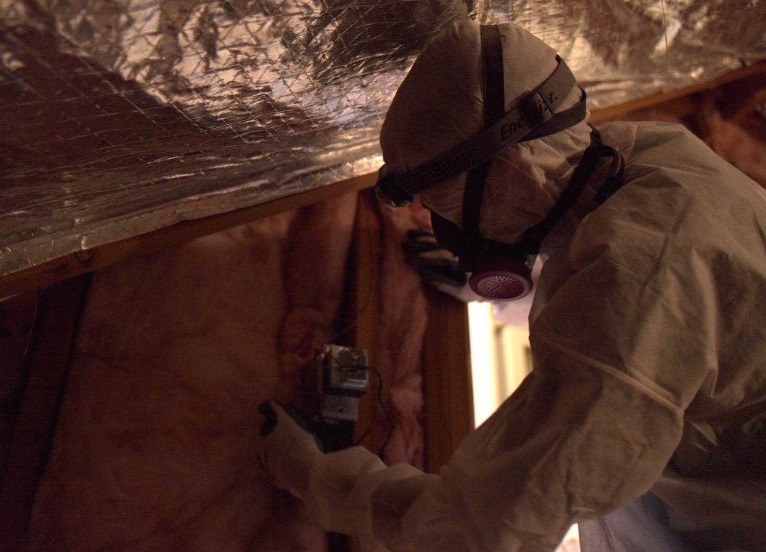 man in white hazard suit and face mask repairing a radient barrier in attic
